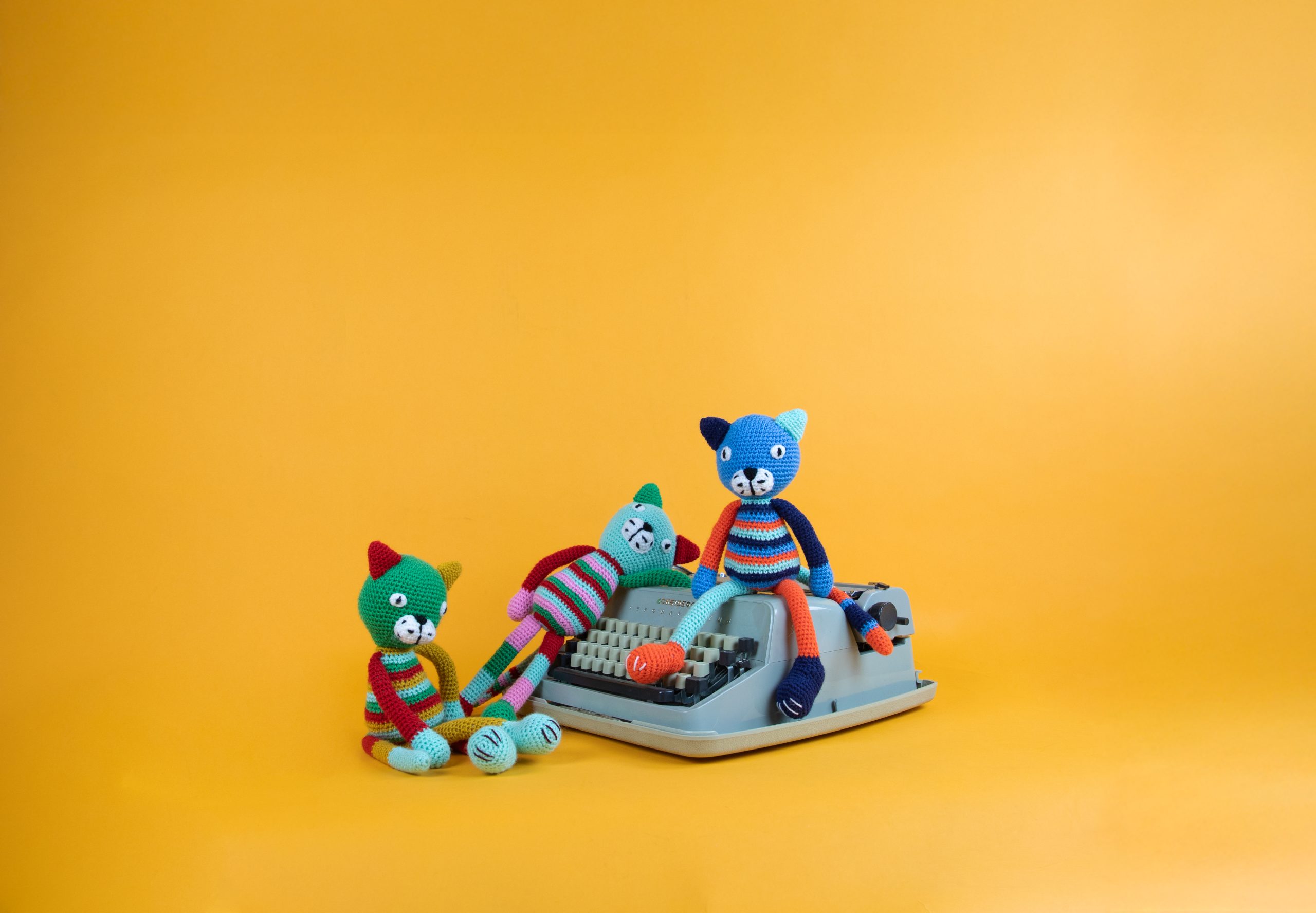 Plaatje van gehaakte katjes-poppetjes op een typemachine tegen een gele achtergrond